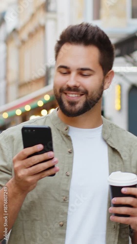 Happy smiling man use smartphone typing text messages browsing internet social media web app working chatting online enjoying morning to-go coffee hot drink outdoor. Boy tourist walking in city street