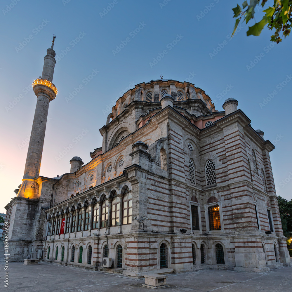 Fototapeta premium Laleli Mosque, or Laleli Camii, a historic Ottoman imperial mosque, illuminated at dusk in Istanbul, Turkey. Features its grand dome, minaret, and unique striped facade under a clear sky.