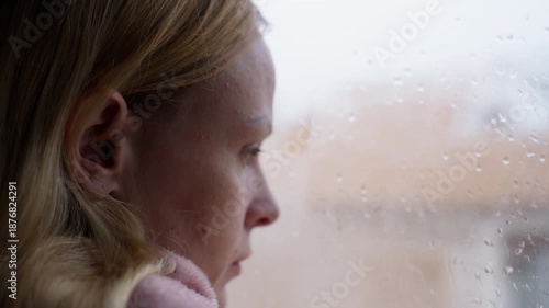 Close up profile of melancholic woman with blonde hair look out window on cold, rainy day, feeling lonely and depressed as reflects on  mental health and sadness
