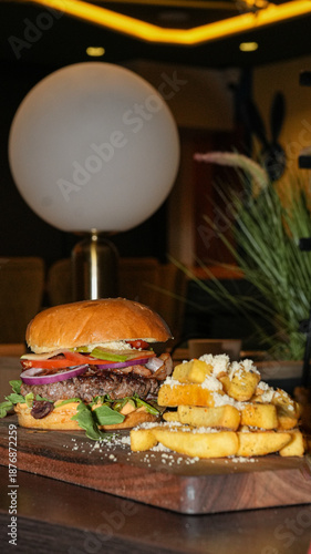 Gourmet beef burger with fresh vegetables served with crispy fries on wooden board in modern steakhouse restaurant, moody food photography