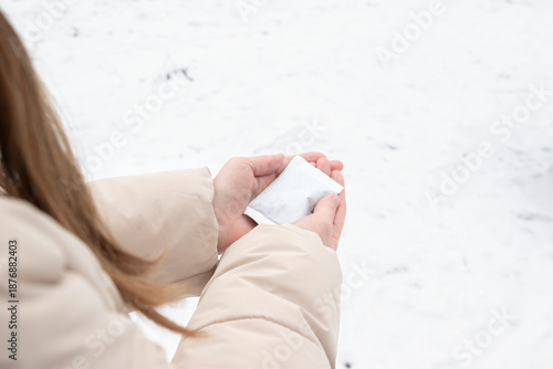 Woman holding a disposable hand warmer while standing outdoors in winter. Concept of cold weather readiness, thermal comfort, outdoor lifestyle, seasonal protection.