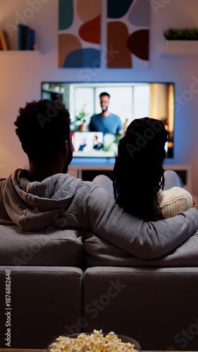 Couple Video Conferencing At Home - A couple is sitting on a sofa in their living room watching a video conference on the TV.