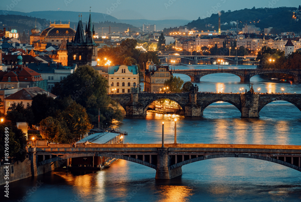 Obraz premium Cityscape At Dusk With Glowing River Bridges, Warm Streetlights Shine On Peaceful Vltava River Arches