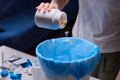 Responsible medication disposal in residential living space, An individual safely discards expired tablets from open containers into trash in living room setting