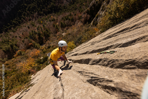A man is climbing a rock wall with a yellow shirt and a white helmet