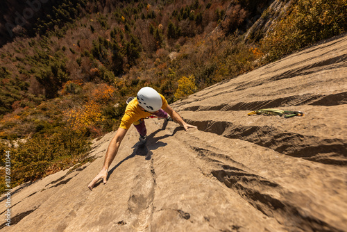 A man is climbing a rock wall with a yellow shirt and white helmet