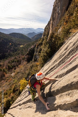 A woman is climbing a rock wall with a red and white harness