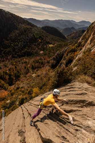 A person is climbing a rock face with a yellow shirt and a white helmet