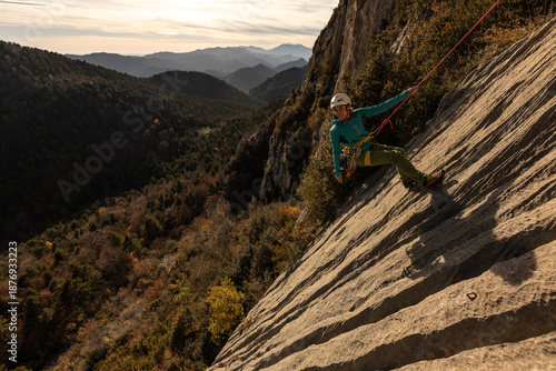 A woman is climbing a rock wall with a green shirt and a yellow helmet