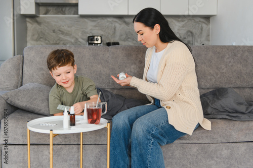 Mother giving medicine to child on sofa at home