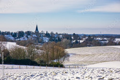 view to the catholic church of homberg over the snow-covered fields in winter at sunlight
