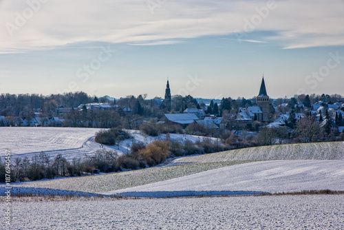 view to the catholic and protestant church of homberg over the snow-covered fields in winter at sunlight