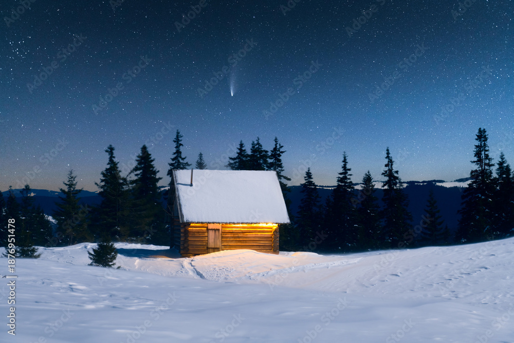 Obraz premium Calm winter landscape with glowing wooden house in snowy mountains. Christmas holiday and winter vacations concept