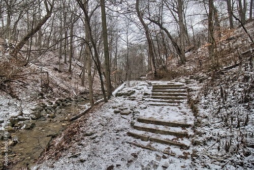 Partially covered in light snow, stone steps along a hiking trail lead through forest ravine on a winter day at Seven Bridges Park in South Milwaukee, Wisconsin.