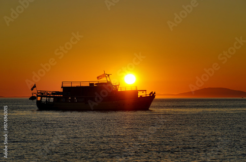 Silhouette of touristic boat on the sea under orange sunset sky