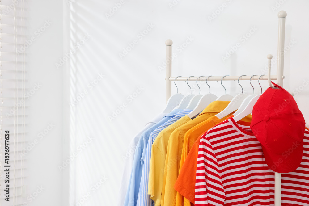 Obraz premium Different clothes and baseball cap hanging on rack near white wall indoors, closeup. Space for text