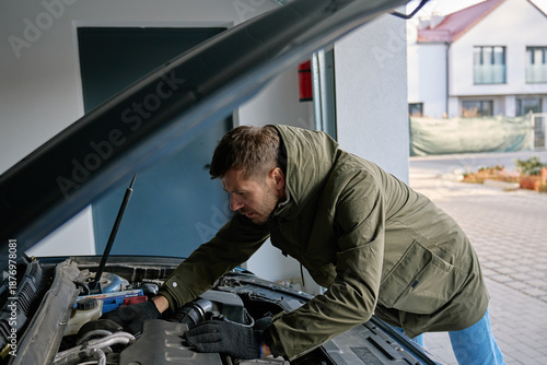 Man inspecting car engine under open hood in residential garage