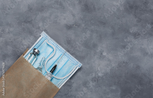 A paper bag with a medical mask, a medical syringe and medicine in ampoules.