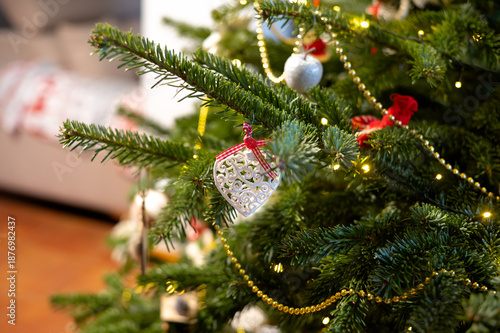 Part of a natural Christmas tree decorated with ornaments in a home interior. Cozy home atmosphere, New Year and Christmas celebration, family holiday, traditions and festive mood.