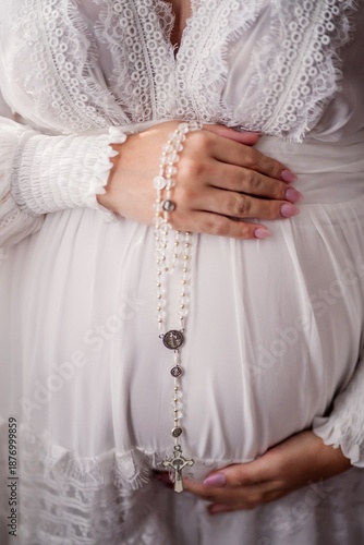 A pregnant woman's hand holding her belly with a rosary.