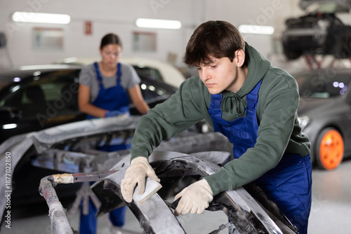 Canvas Print Young professional auto body technician in blue overalls and casual green hoodie