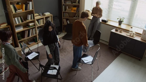 High angle shot of teenage students guided by with female therapist walking in psychotherapy room then sitting on chairs to fill out mental health tests