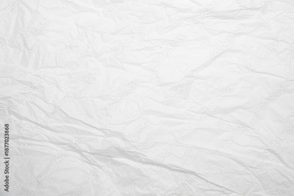 Fototapeta premium Primer plano de hoja de papel blanco con arrugas, pliegues y dobleces sobre superficie texturizada.imperfección y reutilización, simbolizando fragilidad, memoria y naturaleza táctil del material.