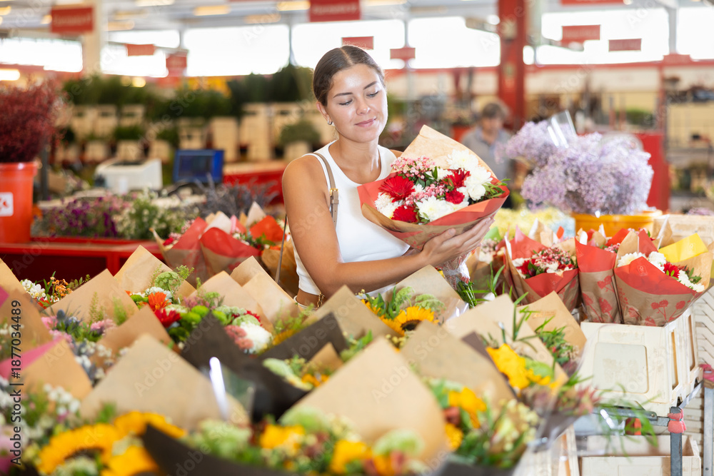 Fototapeta premium Happy young girl buyer holding bouquet of flowers in large plants market