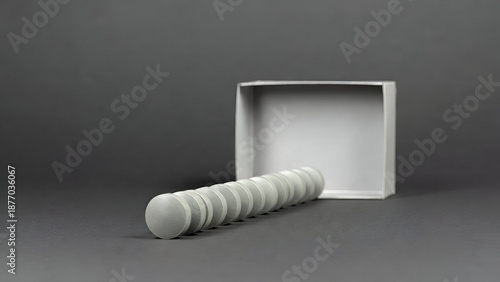 Gray round tablets arranged in line near open blank box on dark background illustrating minimal pharmaceutical product presentation and medication dosage concept
