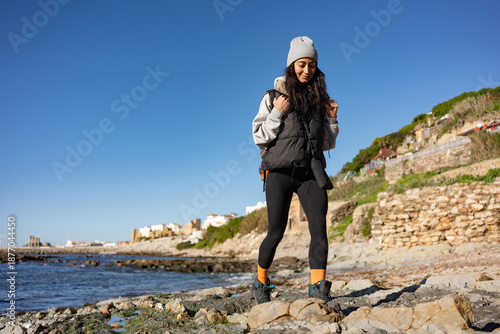 Billede på lærred Young female hiker walking on rocky seashore with backpack, coastal travel lifes