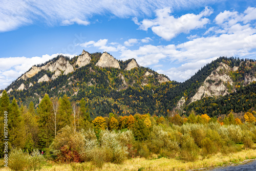 Scenic autumn mountain landscape with Trzy Korony peak and colorful forest in the Pieniny Mountains, Poland. Beautiful nature view under blue sky with clouds.