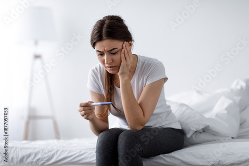 Photos Depressed sad unhappy young pretty european woman looking at negative home test sitting on bed in bedroom interior alone, free space