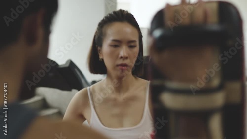 Focused woman training boxing with coach using target pads at gym, showcasing determination, physical strength, self-defense skills, and personal empowerment through fitness.