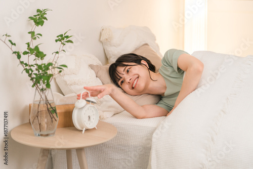 Slika na platnu Young Asian woman waking up in the morning and turning off the alarm clock