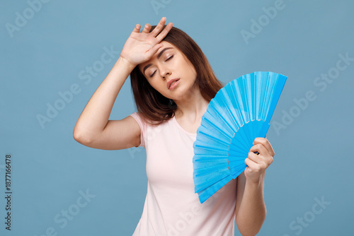 Принти на полотні Upset millennial lady using hand fan over blue studio background, touching her forehead, closing eyes