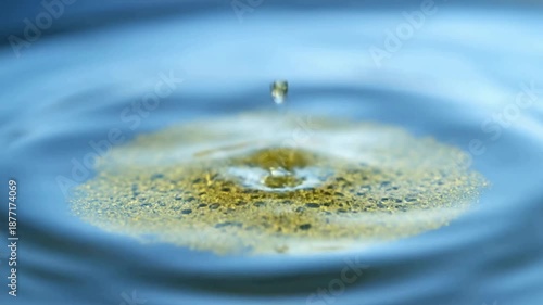 Yellow Liquid Droplets Falling into Blue Water Surface with Ripples and Splashes in Slow Motion