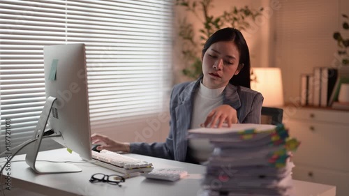 A woman is sitting at a desk with a computer monitor in front of her. She is wearing a blue jacket and white shirt