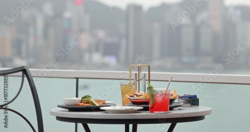 Outdoor dining table with delicious food and refreshing cocktails, overlooking a vibrant city skyline and harbor. A concept of luxury dining, urban lifestyle, travel, hospitality, and fine cuisine.