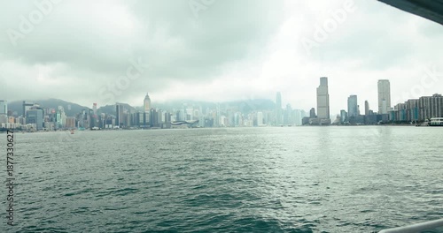Panoramic view of Hong Kong skyline from Victoria Harbour. Modern skyscrapers under cloudy sky. Urban landscape with misty mountains. Commercial travel and business concept. Hong Kong, 15 Apr 2025