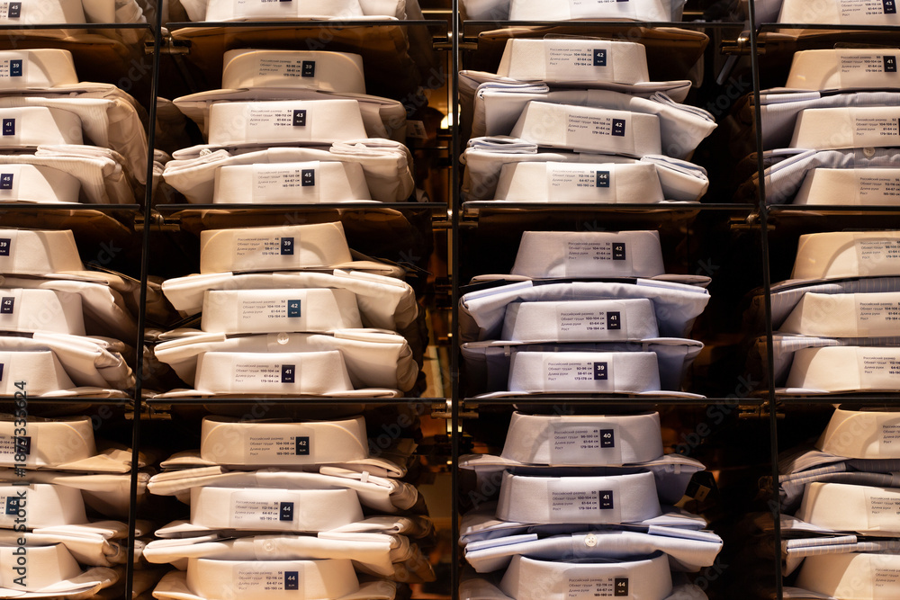 Fototapeta premium Shelf with folded shirts of various sizes. Symmetrical photo of premium shirts for business person. Buying new shirt at clothing store. Choosing quality clothing for classic outfit