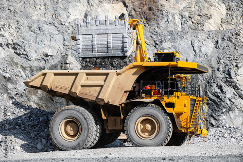 Canvas Print Large quarry excavator Loading gold ore into yellow dump truck for transportation to mining processing plant