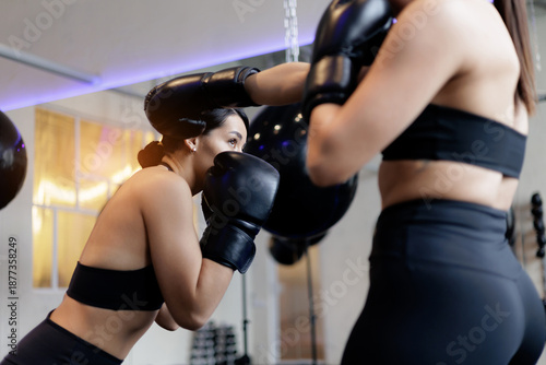 Fotografie Two female adults boxing in gym, sport fitness sparring session with coach