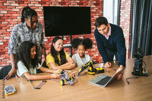 Foto Three diverse students and two inclusive teachers collaborate on a robotics activity using electronics and a laptop, promoting STEM education, teamwork, and hands-on learning in a dynamic classroom