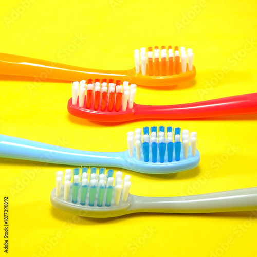 Vibrant toothbrushes in red, orange, blue, and grey arranged on a sleek yellow background, evoking a sense of cleanliness and oral health, Daily routine concept photography