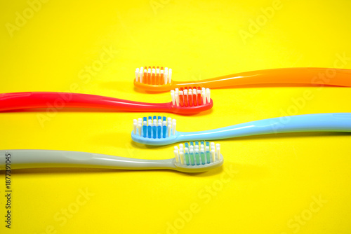 Vibrant toothbrushes in red, orange, blue, and grey arranged on a sleek yellow background, evoking a sense of cleanliness and oral health, Daily routine concept photography