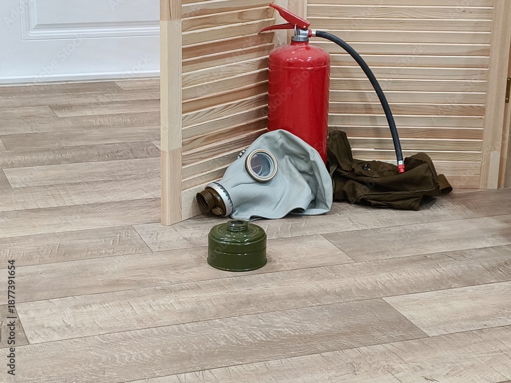 Fototapeta premium Red fire extinguisher with a gas mask and a filter next to a wooden screen. Emergency preparedness and safety equipment for security.