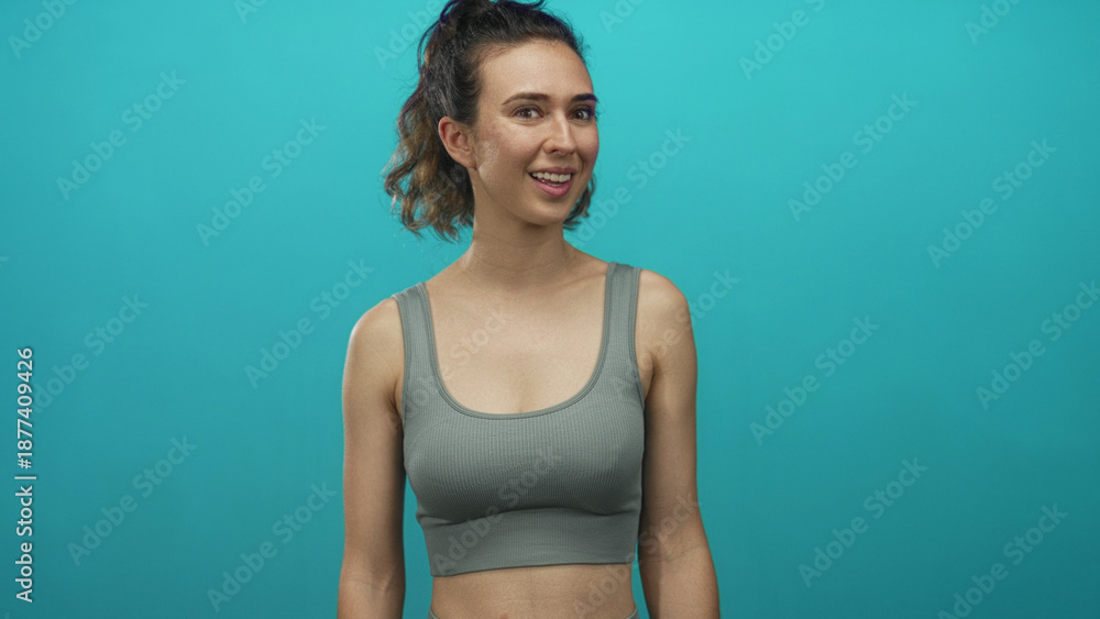 Fototapeta premium Young woman bare chest and midriff turns head sideways in turquoise studio with ponytail; serenity.