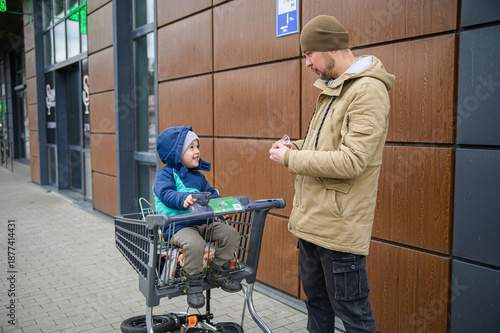 Father and son spending time together during a winter grocery trip, walking with a shopping cart, sharing snacks, and enjoying everyday family moments outdoors near a store.