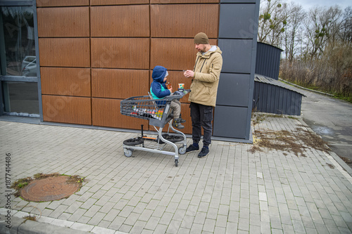 Father and son spending time together during a winter grocery trip, walking with a shopping cart, sharing snacks, and enjoying everyday family moments outdoors near a store.