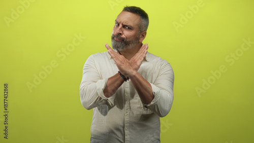 Konstfotografi Middle aged hispanic man with grey hair and beard crossing forearms in an x gesture in lime green studio; rejection caution boundary
